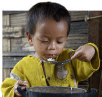Ein Junge sitzt vor einem Topf und löffelt Reis.