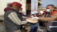 An aid worker hands over loaves of bread wrapped in foil to a man.