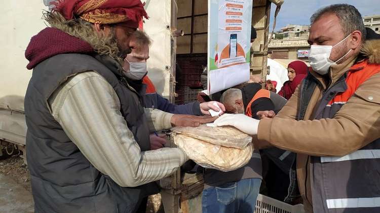 An aid worker hands over loaves of bread wrapped in foil to a man.