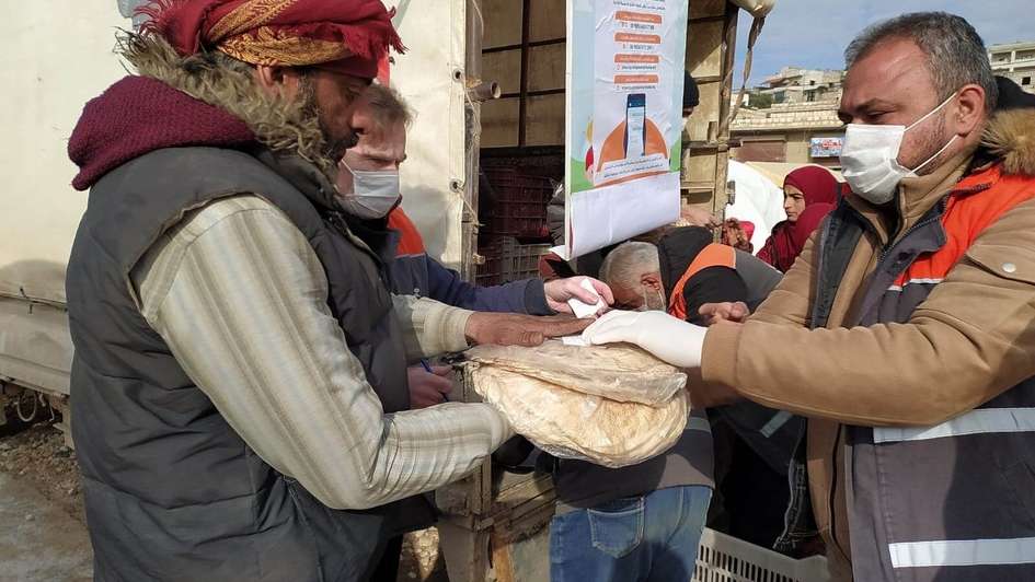 Ein Mitarbeiter einer Hilfsorganisation übergibt in Folie verpackte Brote an einen Mann