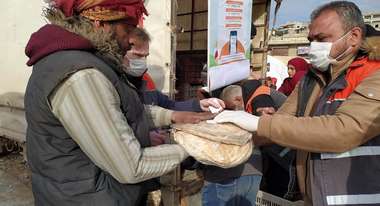 Ein Mitarbeiter einer Hilfsorganisation übergibt in Folie verpackte Brote an einen Mann