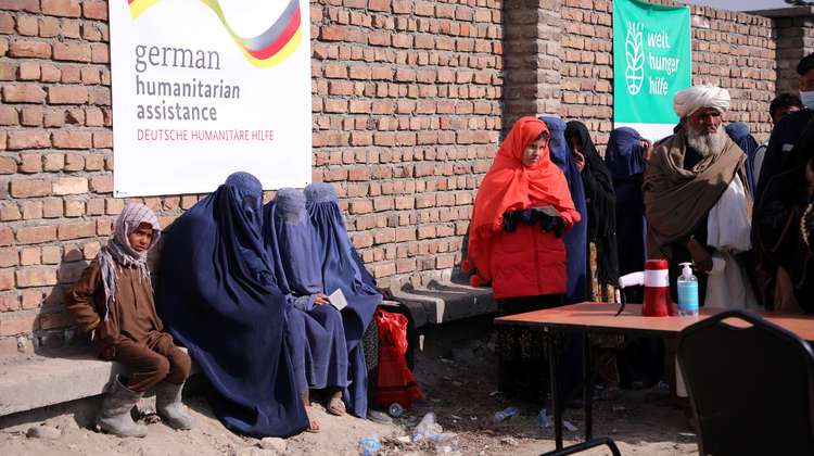 Verschleierte Frauen warten bei einer Lebensmittelverteilung. Im Hintergrund sind Banner mit Welthungerhilfe-Logo und von German Humanitarian Assisstance zu sehen.