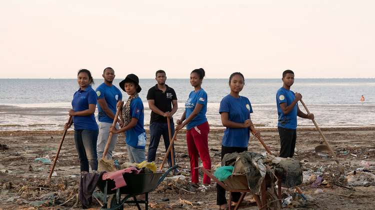 Ein Team aus sieben Personen mit Schubkarren und Schaufeln beseitigt Müll an einem Strand.