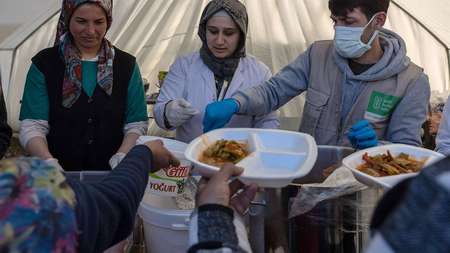 Zwei Frauen und ein Mann stehen in einem Zelt und verteilen Mahlzeiten.