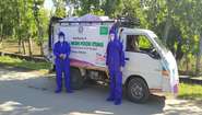 Zwei Männer in Schutzausrüstung stehen vor einem Kleinbus der Welthungerhilfe.