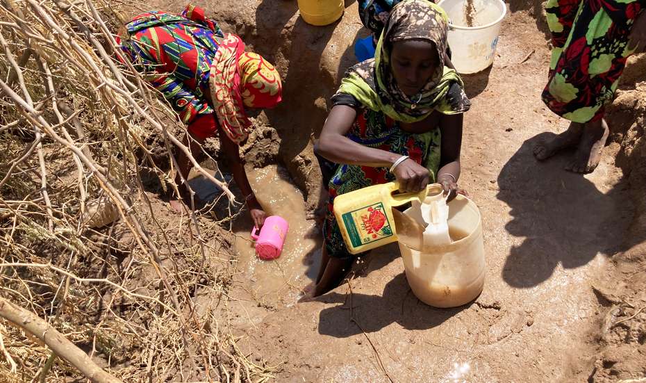Mehrere Frauen holen mit gelben Kanistern Wasser aus einem Erdloch.