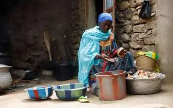 Frau sitzt vor mehreren Schüsseln und verarbeitet Hirse.