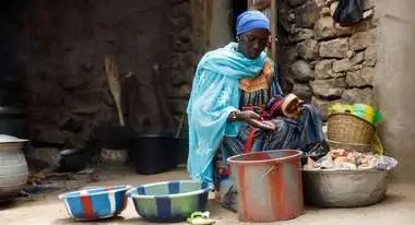 A woman sits in front of several bowls and processes millet.