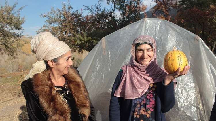 Zwei Frauen stehen vor einem Gewächshause. Eine hält einen Kürbis in der Hand, Tadschikistan 2021.