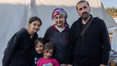 Erdbeben in der Türkei: Eine Familie steht vor einem Zelt, sie alle schauen in die Kamera.