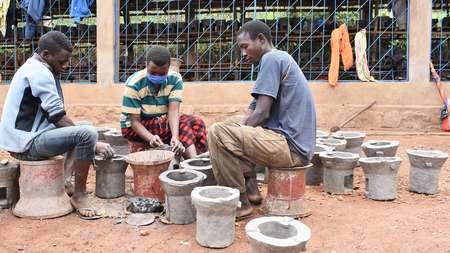Drei junge Menschen sitzen sich gegenüber und töpfern Öfen, Burundi 2021 