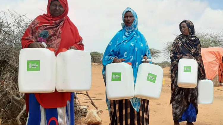 Three women stand side by side, each holding two water containers.