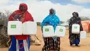 Three women stand side by side, each holding two water containers.