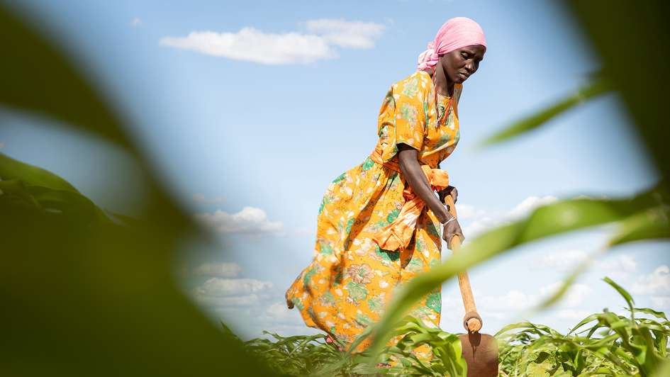 Eine Frau in Kenia beackert mit einer Hacke ein Feld.