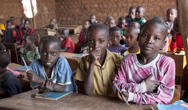 Drei Jungen sitzen im Vordergrund einer Schulklasse in Burundi
