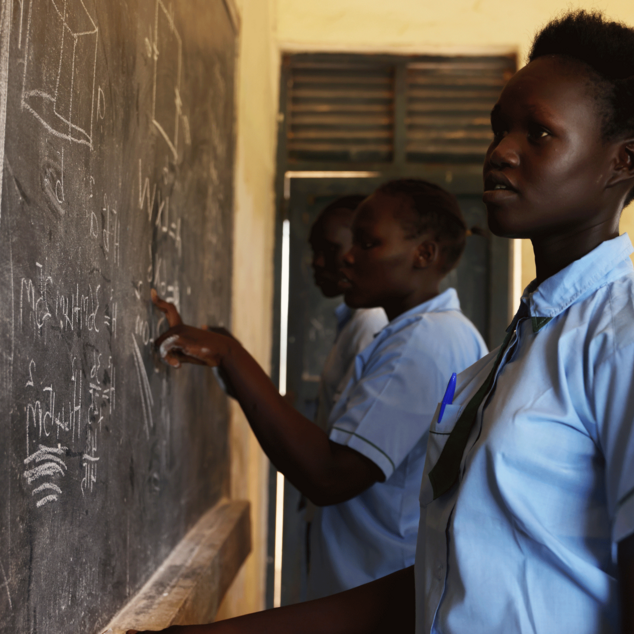 Bild aus einem Projekt im Südsudan mit Schulspeisungen, ein Mädchen steht an einer Schultafel.