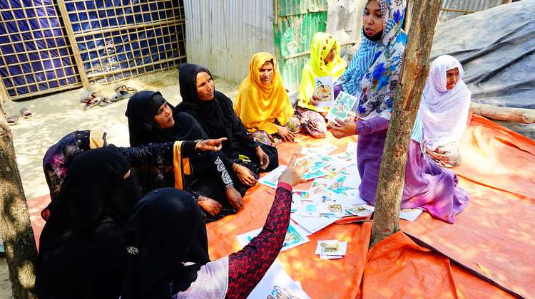 Rohingya women sitting on the floor looking and pointing at hygiene training cards