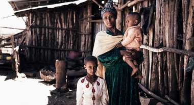 Eine Frau steht mit ihren beiden Kindern vor einer Holzhütte, Äthiopien.