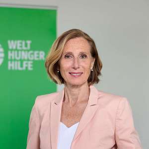 Simone Pott, Head of Communications der Welthungerhilfe, steht vor dem Logo der Organisation.