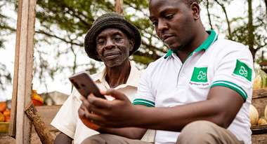 Zwei Kleinbauern schauen in ihr Smartphone und beschäftigen sich mit der Landwirtschafts-App AgriShare, Uganda 2021.