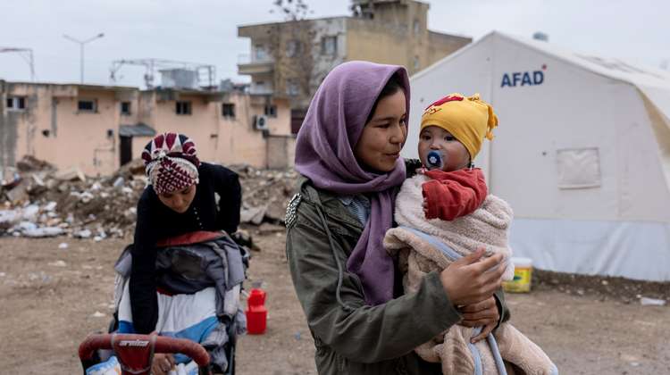 Ein junges Mädchen hält vor einem Flüchtlingszelt ein Baby im Arm