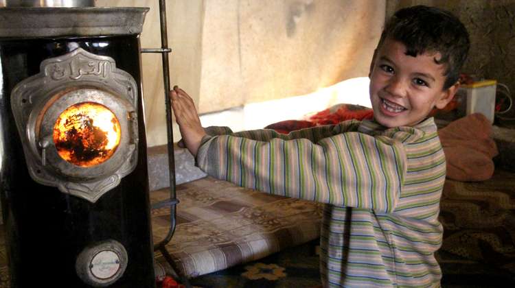 A boy stretches his hands towards a stove whilst smiling at the camera