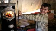A boy stretches his hands towards a stove whilst smiling at the camera
