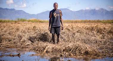 A Malawian farmer standing in his flooded field, looking at the camera.