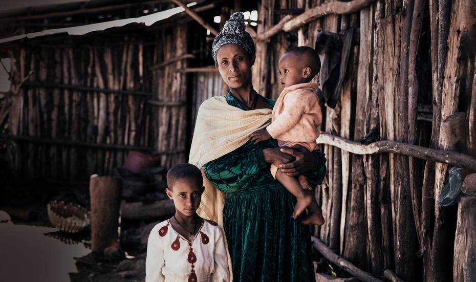 Eine Mutter mit ihren beiden Kindern; eines trägt sie auf dem Arm.